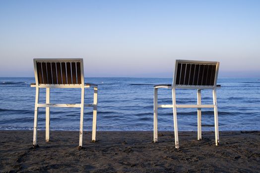 Chairs stand in the sand.Two empty chairs stand on beach in evening with view on marine sunset.