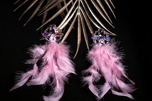 Jewelry. Women's jewelry.Earrings of pink feathers on a black background close-up, selective focus.