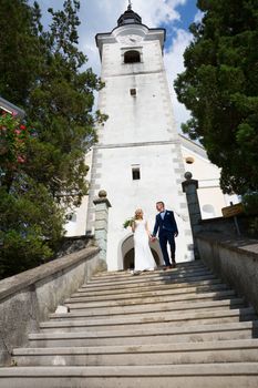 The Kiss. Bride and groom holding hands walking down the staircase in front of a small local church. Stylish wedding couple kissing.