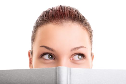 Close up shot of a pretty young girl hiding behind an open book looking away, isolated on white background.