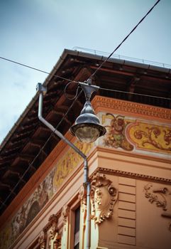 Old vintage street lamp on crossing aerial wires hanging above the street with a beautiful old building with ornamental architecture in the background. View from below. The city center of Budapest.