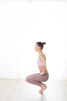 Portrait of gorgeous active sporty young woman practicing yoga in studio. Beautiful girl practice Utkatasana, awkward yoga pose. Healthy active lifestyle, working out in gym.