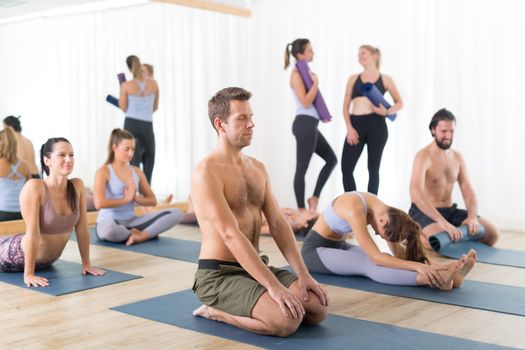 Group of young sporty attractive people in yoga studio, relaxing and socializing after hot yoga class. Healthy active lifestyle, working out indoors.