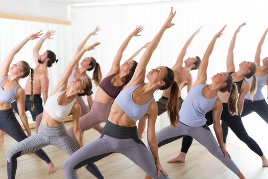 Group of young authentic sporty attractive people in yoga studio, practicing yoga lesson with instructor. Healthy active lifestyle, working out in gym.