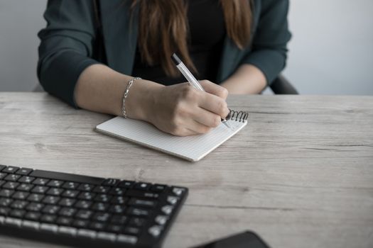 Business woman writing something in notebook. Start-up woman entrepreneur student studying writing note at workplace near computer. A woman's hand writing down on a white blank notebook on table