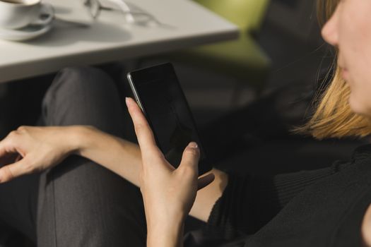 Young business woman uses phone. Good looking brunette female uses online banking on smart phone to transfer money from credit card. Girl using smart phone and chatting with business partners