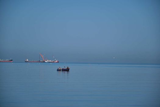 The Small Fisherman Boat in the Sea. A small fisherman boat floating on the sea near the seashore with Cargo ship background