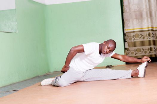 Young man spread legs sitting on a carpet stretching in the gym. Thigh fortifying movement.