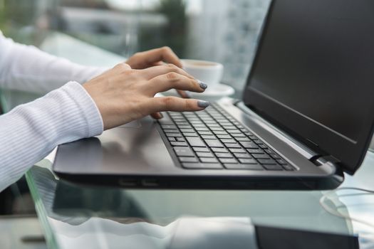 A woman is working by using a laptop computer on table. Hands typing on a keyboard. Female businessman is typing on a laptop keyboard sitting in cafe