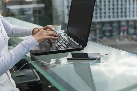 A woman is working by using a laptop computer on table. Hands typing on a keyboard. Female businessman is typing on a laptop keyboard sitting in cafe