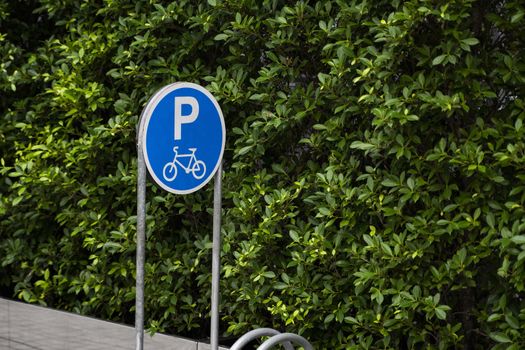 Empty stainless steel bicycle parking rack with a sign of bicycle parking with a green plants on a wall