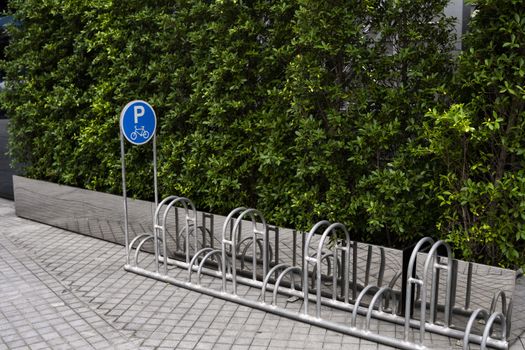 Empty stainless steel bicycle parking rack with a sign of bicycle parking with a green plants on a wall