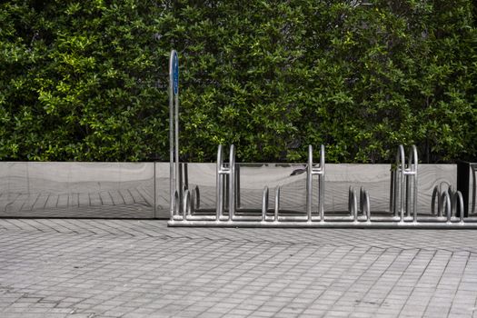 Empty stainless steel bicycle parking rack with a sign of bicycle parking with a green plants on a wall