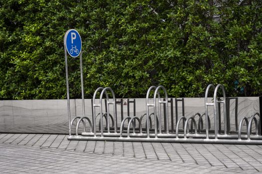 Empty stainless steel bicycle parking rack with a sign of bicycle parking with a green plants on a wall