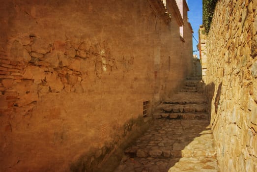 Spain, Tossa de Mar, cobbled street, staircase and stone wall in medieval Old Town - Vila Vella. Photo in old color image style.