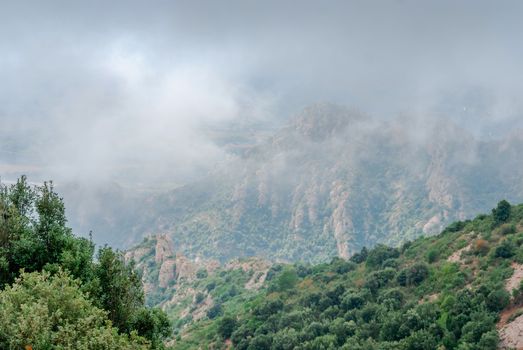 Hazy unusual mountains with green trees and cloudy sky near Montserrat Monastery,Spain. Catalonia
