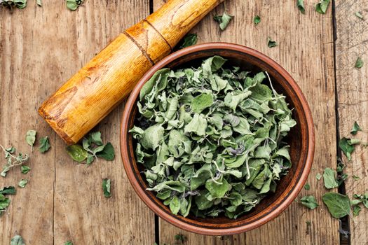 Bowl of dried oregano leaves on wooden background