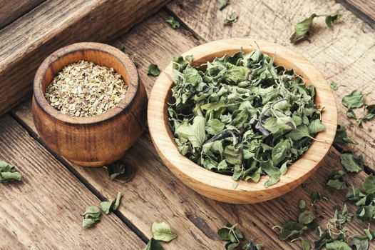 Bowl of dried oregano leaves on wooden background