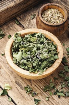 Bowl with dried oregano on old wooden table