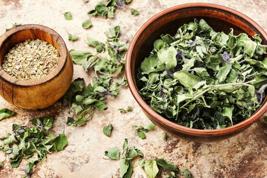 Bowl of dried oregano leaves on wooden background