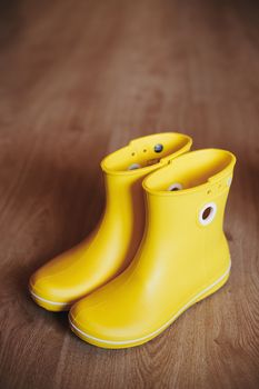 Yellow rubber boots isolated on wooden background.