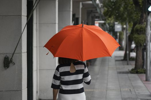 Back view of woman with orange umbrella walking on a street