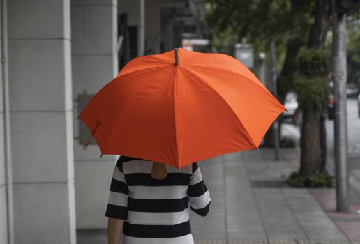 Back view of woman with orange umbrella walking on a street