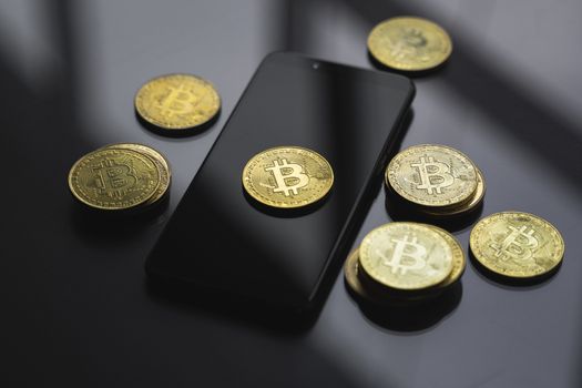 Golden bitcoin coin on a smartphone with a lot of bitcoins coins on a table. Virtual cryptocurrency concept. Mining of bitcoins online bussiness. Bitcoins trading