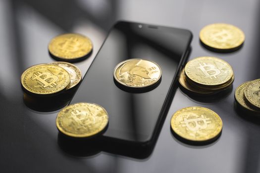 Golden Titan bitcoin coin on a smartphone with a lot of bitcoins coins on a table. Virtual cryptocurrency concept. Mining of bitcoins online bussiness. Bitcoins trading