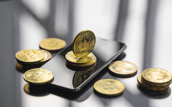 Golden bitcoin coin on a smartphone with a lot of bitcoins coins on a table. Virtual cryptocurrency concept. Mining of bitcoins online bussiness. Bitcoins trading