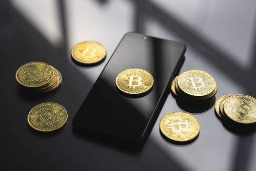 Golden bitcoin coin on a smartphone with a lot of bitcoins coins on a table. Virtual cryptocurrency concept. Mining of bitcoins online bussiness. Bitcoins trading