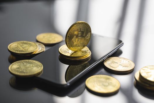Golden bitcoin coin on a smartphone with a lot of bitcoins coins on a table. Virtual cryptocurrency concept. Mining of bitcoins online bussiness. Bitcoins trading