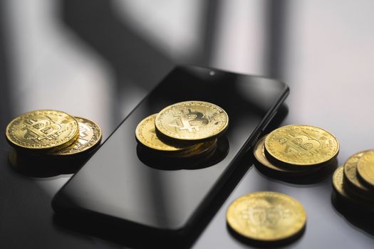 Golden bitcoin coin on a smartphone with a lot of bitcoins coins on a table. Virtual cryptocurrency concept. Mining of bitcoins online bussiness. Bitcoins trading