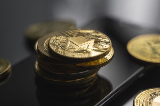 Stack of golden Monero bitcoin coin on a smartphone with a lot of bitcoins coins on a table. Virtual cryptocurrency concept. Mining of bitcoins online bussiness. Bitcoins trading