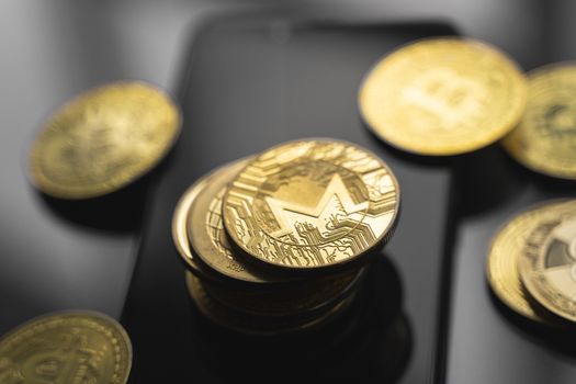 Stack of golden Monero bitcoin coin on a smartphone with a lot of bitcoins coins on a table. Virtual cryptocurrency concept. Mining of bitcoins online bussiness. Bitcoins trading