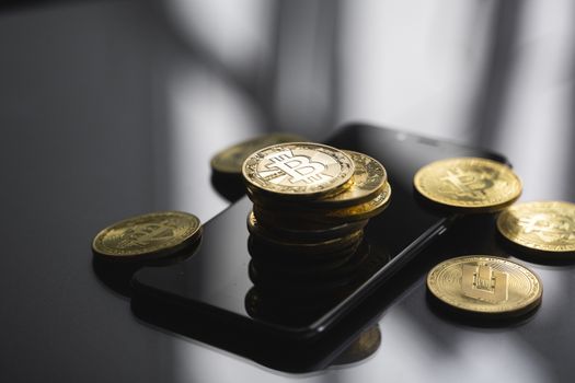 Golden bitcoin coin on a smartphone with a lot of bitcoins coins on a table. Virtual cryptocurrency concept. Mining of bitcoins online bussiness. Bitcoins trading