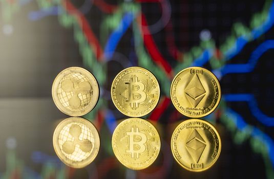 Cryptocyrrency and virtual money concept. Golded bitcoin, ethereum and ripple coins with chart of growing and falling valuance of a cryptocurrency. Mining or blockchain technology