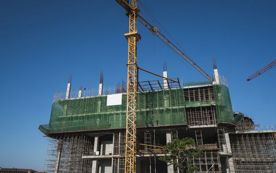 Crane and building construction site against blue sky. Metal construction of unfinished building on construction. Tower Crane use for building of multi storage building