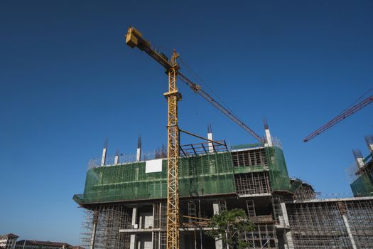 Cranes and building construction site against blue sky. Metal construction of unfinished building on construction. Tower Crane use for building of multi storage building