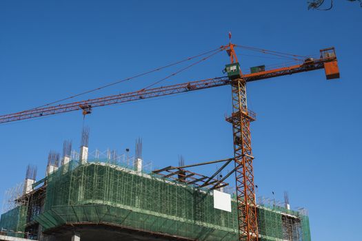 Crane and building construction site against blue sky. Metal construction of unfinished building on construction. Tower Crane use for building of multi storage building