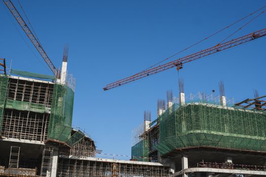 Cranes and building construction site against blue sky. Metal construction of unfinished building on construction. Tower Crane use for building of multi storage building