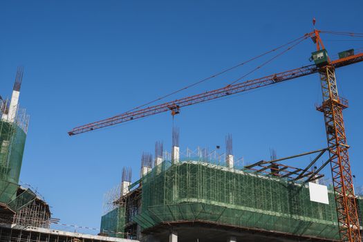 Crane and building construction site against blue sky. Metal construction of unfinished building on construction. Tower Crane use for building of multi storage building