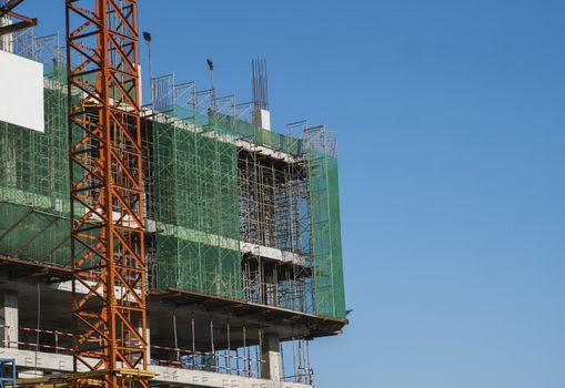 Crane and building construction site against blue sky. Metal construction of unfinished building on construction. Tower Crane use for building of multi storage building