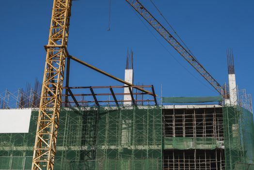 Crane and building construction site against blue sky. Metal construction of unfinished building on construction. Tower Crane use for building of multi storage building