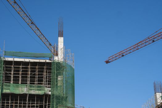 Crane and building construction site against blue sky. Metal construction of unfinished building on construction. Tower Crane use for building of multi storage building