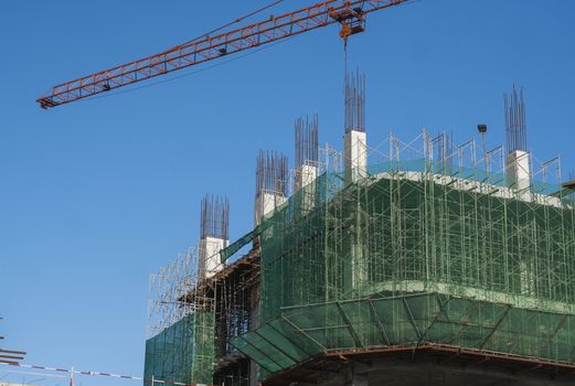 Crane and building construction site against blue sky. Metal construction of unfinished building on construction. Tower Crane use for building of multi storage building