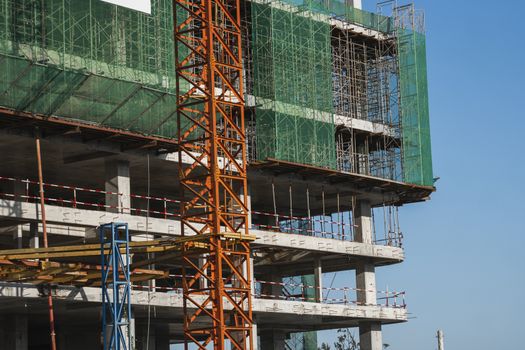 Crane and building construction site against blue sky. Metal construction of unfinished building on construction. Tower Crane use for building of multi storage building