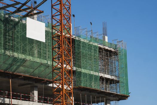 Crane and building construction site against blue sky. Metal construction of unfinished building on construction. Tower Crane use for building of multi storage building