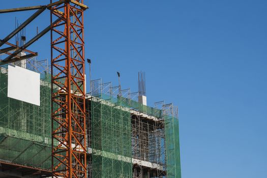 Crane and building construction site against blue sky. Metal construction of unfinished building on construction. Tower Crane use for building of multi storage building
