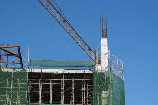 Crane and building construction site against blue sky. Metal construction of unfinished building on construction. Tower Crane use for building of multi storage building